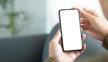 Mockup image blank white screen cell phone.women hand holding texting using mobile on sofa photo