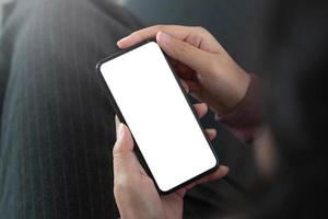 imagen de la maqueta teléfono celular de pantalla blanca en blanco. mano de mujer sosteniendo mensajes de texto usando el móvil en el sofá. foto