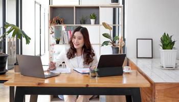 Beautiful young asian woman sitting at coffee shop using laptop. Happy young businesswoman sitting at table in cafe with tab top computer. photo