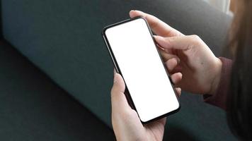 imagen de maqueta de teléfono celular de pantalla blanca en blanco. Mano de mujer sosteniendo mensajes de texto usando el móvil en el sofá foto