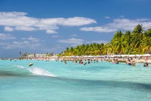 People swimming near white sand beach with umbrellas, bungalow bar and cocos palms, turquoise caribbean sea, Isla Mujeres island, Caribbean Sea, Cancun, Yucatan, Mexico photo