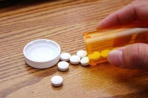 A man's hand is taking pills from an orange pill bottle on a wooden table, medicine pill on wooden table. photo