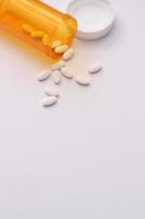 Oval pills and orange pill bottles were spread out on the white tabletop. photo