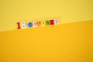 October 18 on a yellow, paper background with wooden and multicolored letters with space for text. photo