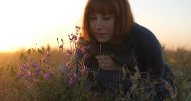 joven pelirroja con hermoso vestido boho relajándose en el campo durante la puesta de sol nublada, mujer al aire libre con ramo en las manos foto