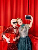 dos mujeres mayores en la fiesta haciendo selfie sosteniendo el celular en el palo selfie. fiesta, celebración, concepto de tecnología. foto