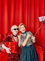 Two senior women at the party making selfie holding cellphone on selfie stick. Party, celebration, technology concept photo