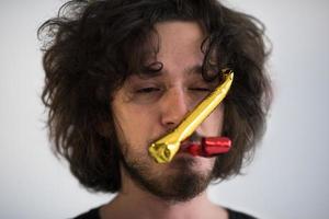 Portrait of a man in party hat blowing in whistle photo