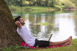 man using a laptop computer on the bank of the river photo