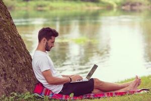 man using a laptop computer on the bank of the river photo