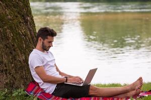 man using a laptop computer on the bank of the river photo