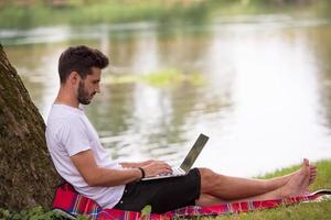 man using a laptop computer on the bank of the river photo