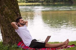 man using a laptop computer on the bank of the river photo