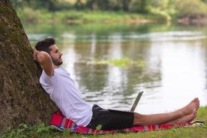 man using a laptop computer on the bank of the river photo