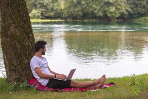 man using a laptop computer on the bank of the river photo