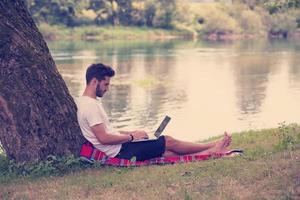 man using a laptop computer on the bank of the river photo