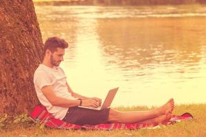 man using a laptop computer on the bank of the river photo