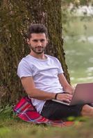 man using a laptop computer on the bank of the river photo
