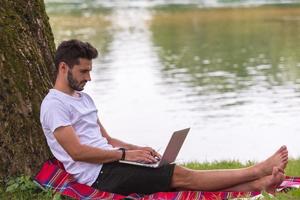 man using a laptop computer on the bank of the river photo