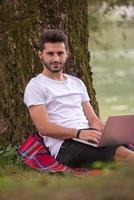 man using a laptop computer on the bank of the river photo