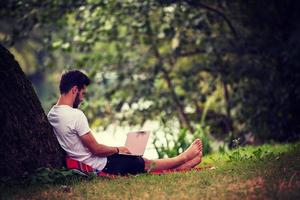 man using a laptop computer on the bank of the river photo