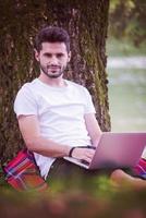 man using a laptop computer on the bank of the river photo