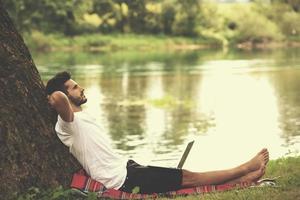 man using a laptop computer on the bank of the river photo