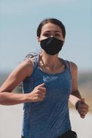Determined fitness woman in short clothes wearing red protective face mask running outdoors in the city during coronavirus outbreak. Covid 19 and physical jogging activity, sport and fitness. photo