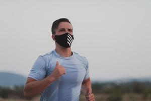 hombre de fitness con ropa deportiva mojada con mascarilla protectora negra corriendo al aire libre en la ciudad durante el brote de coronavirus. covid 19 y actividad física de jogging deporte y fitness. nueva normalidad foto