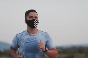 hombre de fitness con ropa deportiva mojada con mascarilla protectora negra corriendo al aire libre en la ciudad durante el brote de coronavirus. covid 19 y actividad física de jogging deporte y fitness. nueva normalidad foto