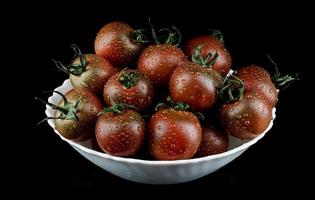 Ripe tomatoes in a white plate are isolated on a black background. Black tomatoes. Cumato tomatoes. photo