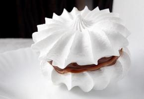 Beautiful white meringues with a silver spoon on a white plate. White cake.