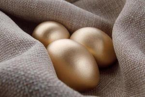 tres huevos de oro en un nido de tejido burdo. foto