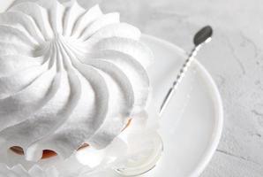 Beautiful white meringues with a silver spoon on a white plate. White cake.