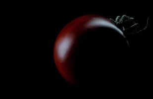 tomate negro sobre un fondo negro. el tomate cherry es cumato sobre un fondo negro. foto