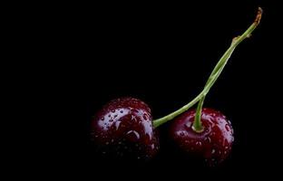 Two ripe cherry berries with drops of water on the peel are isolated on a black background. photo