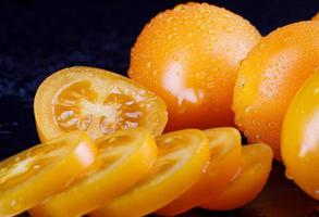 Beautiful whole yellow tomatoes with drops of water on the peel and a cut tomato on a black background.