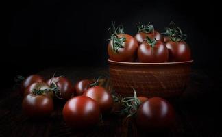 tomates jugosos maduros en un plato de arcilla y junto a él sobre un fondo negro.