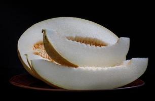 Slices of ripe melon and half melon on a clay plate. photo