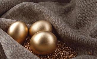 Three golden eggs on gold sand in waves of tissue. photo