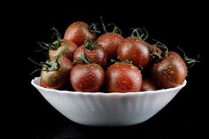 Ripe tomatoes in a white plate are isolated on a black background. Black tomatoes. Cumato tomatoes. photo