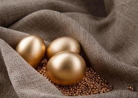 Three golden eggs on gold sand in waves of tissue. photo