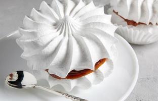 Beautiful white meringues with a silver spoon on a white plate. White cake. photo