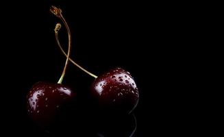 Two cherry berries with drops of water on the peel are isolated on a black background. photo