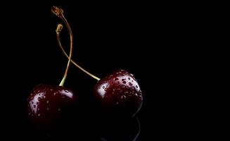 dos bayas de cereza con gotas de agua en la cáscara están aisladas en un fondo negro. foto