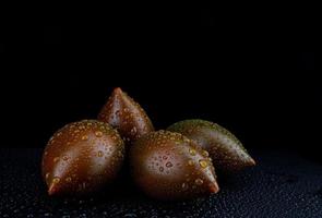 Several ripe cumato tomatoes with drops of water on the peel on a black background. photo