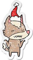 distressed sticker cartoon of a wolf showing teeth wearing santa hat vector