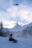 rescue team with a red helicopter rescuing a hurt skier photo