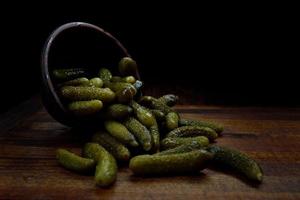 Juicy crispy pickled cucumbers are poured from a clay cup onto a wooden cutting board. Salted cucumbers. photo