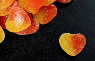 Many marmalade hearts and a separate marmalade heart on black. Marmalade candy in the form of a heart. photo